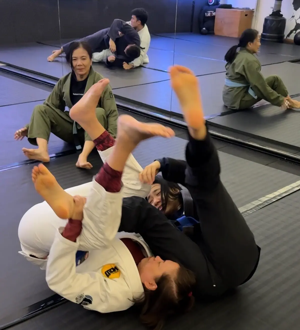 VCBJJ female members live rolling in gi, with a more experienced female member watching and coaching from the background